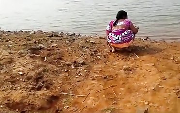 Indian woman peeing in the dirt by a lake